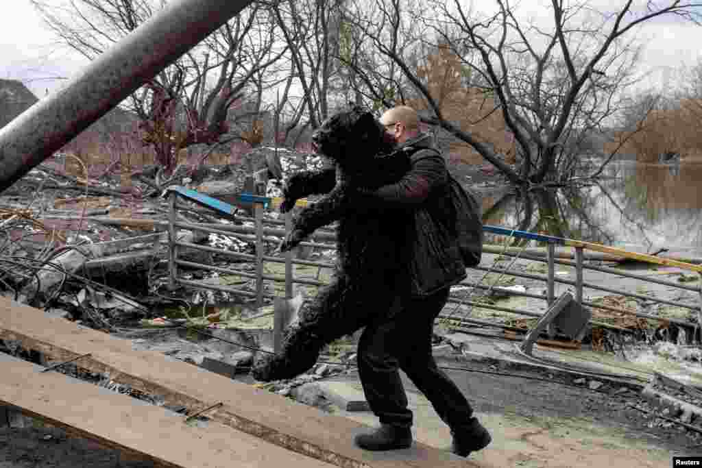 A man carries a dog as he crosses Irpin River in Irpin outside Kyiv, March 9, 2022.