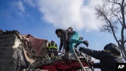 Firefighters help a woman evacuate from an apartment building damaged by shelling in Mariupol, Ukraine, March 10, 2022.