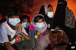 Perempuan dan anak-anak etnis Rohingya duduk di dekat api unggun di pantai setelah perahu mereka terdampar di Pulau Idaman di Aceh Timur, Jumat malam, 4 Juni 2021, setelah meninggalkan kamp pengungsi di Bangladesh. (Foto: AP/Zik Maulana)