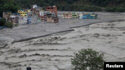 Orang-orang berdiri di atap rumah saat air banjir dari Sungai Melamchi yang meluap memasuki Desa Sindhupalchok, Nepal, 16 Juni 2021. (Foto: REUTERS/Navesh Chitrakar)
