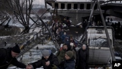 Warga Ukraina melintasi jalur improvisasi di bawah jembatan yang hancur saat melarikan diri dari Irpin, di pinggiran Kyiv, Ukraina, Selasa, 8 Maret 2022. (Foto: AP/Felipe Dana)