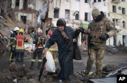 Seorang relawan Pasukan Pertahanan Teritorial Ukraina membantu seorang perempuan menyeberang jalan di Kharkiv, Ukraina, Rabu, 16 Maret 2022. (Foto: AP)