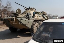 Seorang pengungsi menunggu di dalam mobil saat pengangkut personel lapis baja pasukan pro-Rusia keluar dari pos pemeriksaan selama konflik Ukraina-Rusia di kota pelabuhan selatan yang terkepung Mariupol, Ukraina, 24 Maret 2022. (Foto: REUTERS/Alexander Ermochenko)