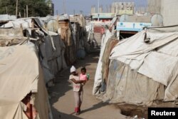 Seorang anak perempuan menggendong anak kecil melalui kemah-kemah sementara untuk para pengungsi (IDP) di Aden, Yaman, 15 Maret 2022. (REUTERS/Fawaz Salman)