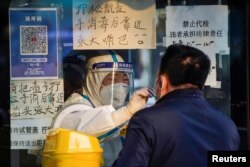 Seorang nakes mengenakan APD mengumpulkan sampel swab dari seorang pria di tempat pengujian asam nukleat, saat wabah virus COVID-19 terus berlanjut di Shanghai, China, 12 Desember 2022. (REUTERS/Aly Song)