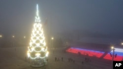 People walk past a Christmas tree decorated for Christmas and the New Year festivities in Mariupol, in Russian-controlled Donetsk region, eastern Ukraine, Dec. 24, 2022.