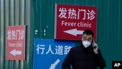一名男子站在街头打电话。他身后的红色指示牌上写着”发热门诊“。自从中国政府出人意料地突然放宽了封控措施之后，各地的感染人数不断增加，使原本就贫乏的医疗资源面临更沉重的压力。