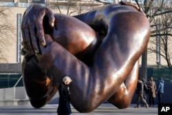 Passers-by walk near the 20-foot-high bronze sculpture "The Embrace," a memorial to Dr. Martin Luther King Jr. and Coretta Scott King, in the Boston Common, Jan. 10, 2023, in Boston.