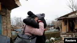 在基辅，一名当地居民在被俄罗斯导弹袭击破坏的房屋与朋友拥抱。(2022年12月29日)