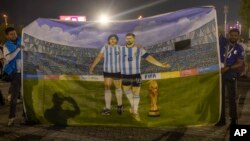 Mohid Data and Aayush Verma, from India, show a huge painting of their Argentine heroes Lionel Messi and Diego Maradona with the World Cup trophy prior to the World Cup soccer match between Poland and Argentina in Doha, Qatar, Nov. 30, 2022.