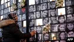 FILE - In this photo taken Jan. 8, 2022, a woman touches victims' portraits as mourners attend an outdoor vigil for the victims of Ukrainian passenger jet flight PS752, which was shot down two years ago over Iran, in Toronto.