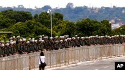 Seorang perempuan berjalan di depan barisan polisi militer, yang bersiap menjaga keamanan sebelum berlangsungnya aksi protes pendukung mantan Presiden Jair Bolsonaro, di Brasilia, Brazil, 11 Januari 2023. (Foto AP/Gustavo Moreno)