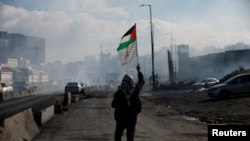FOTO FILE: Seorang pria berjalan dengan membawa bendera Palestina, saat bentrok dengan pasukan Israel dalam aksi protes di dekat Qalandia, Tepi Barat yang diduduki Israel, 27 Desember 2022. (REUTERS/ Mohammad Torokman/File Foto)