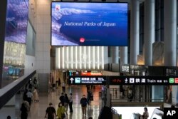 Pengunjung mengenakan masker berjalan di bawah layar yang menampilkan video promosi pariwisata di Jepang, di bandara internasional Narita di Narita, dekat Tokyo, Jumat, 10 Juni 2022. (AP/Shuji Kajiyama)