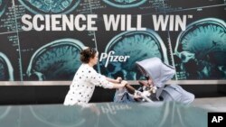 A woman pushes a baby in a stroller past a sign hanging outside Pfizer headquarters in New York, Monday, May 23, 2022. American health officials said Sunday that Pfizer's COVID-19 vaccine appears to be safe and effective for children under 5. (AP Photo/Mary Altaffer)