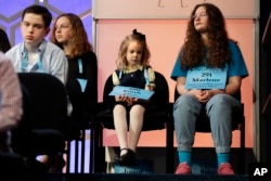 Edith Fuller, 6, of Tulsa, Okla., center, the youngest speller ever in the National Bee, sits next to Marlene Schaff, 14, of Lake Forest, Ill., right, as they wait to compete in the 90th Scripps National Spelling Bee in Oxon Hill, Md., May 31, 2017.
