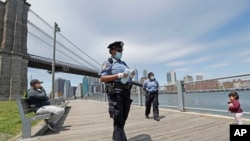 A youngster approaches a team of New York City police officers as they walk with face masks to hand out to anyone who needs or asks for one during the current coronavirus outbreak, Sunday, May 17, 2020, in Brooklyn Bridge Park in New York.