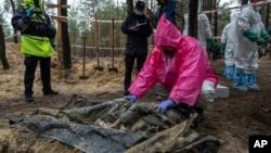 A forensic expert examines the body of a civilian during exhumation in the recently retaken area of Izium, Kharkiv region, Ukraine, Sept. 23, 2022.
