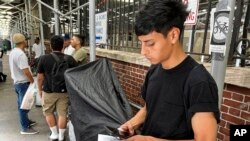 FILE — Dilan Jimenez reads text messages as he stands outside a shelter, after arriving on a chartered bus from Texas earlier in the day, Aug. 10, 2020, in New York.