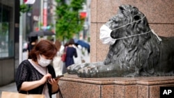FILE - A shopper wearing a face mask checks her mobile phone beside a masked lion statue of a department store in Ginza shopping district in Tokyo, Aug. 30, 2022.