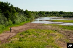 A cyclist bikes through a mostly dry Rio Grande riverbed Wednesday, July 27, 2022, in Albuquerque, N.M. AP Photo/Brittany Peterson)