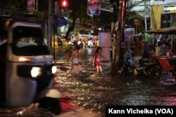 កុមារី​ពីរនាក់​កំពុង​ដើរ​កាត់​ទឹកដែល​លិចត្រង់​ស្តុប​ផ្លូវ​លេខ​១៣៩ កែង​ផ្លូវ​ហ្សាល​ដឺហ្គោល រាជធានី​ភ្នំពេញ​ នៅ​ថ្ងៃទី២៣ ខែ​មិថុនា ឆ្នាំ​២០២២។ (កាន់ វិច្ឆិកា/វីអូអេ)