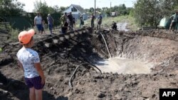 A boy looks at communal service employees working around a crater after a Russian missile strike in the town of Kostiantynivka, in the Donetsk region, on July 16, 2022. 