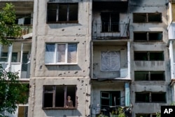 Ida Svystunova, 89, looks out the damaged room adjoining her apartment from a May rocket attack in Sloviansk, Donetsk region, eastern Ukraine, Sunday, Aug. 7, 2022. (AP Photo/David Goldman)