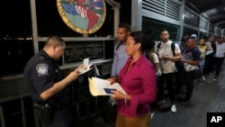 FILE - A U.S. Customs and Border Protection officer checks the documents of migrants who are on their way to apply for asylum in the United States, on International Bridge 1 as they depart Nuevo Laredo, Mexico, Sept. 17, 2019.