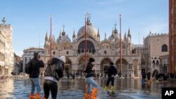 Sejumlah orang tampak berjalan melintasi alun-alun St Mark di Venesia, Italia, yang digenangi oleh banjir rob pada 4 Desember 2021. (Foto: AP/Luigi Costantini)