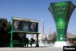 Arhiva - Ljudi sede ispod postera lidera Hutija u Sani, Jemen, 7. aprila 2022.