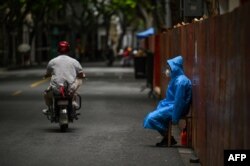 Seorang pekerja duduk di sebelah pagar yang didirikan untuk menutup area perumahan di tengah lockdown COVID-19 di distrik Huangpu, Shanghai. (Foto: AFP)