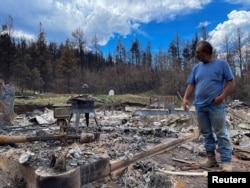 FILE - Daniel Encinias stands next to the ruins of his home destroyed by the Hermits Peak Calf Canyon fire in Tierra Monte, New Mexico, June 9, 2022.