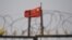 FILE - The Chinese flag flies behind razor wire at a housing compound in Yangisar, south of Kashgar, in China's western Xinjiang region, June 4, 2019.