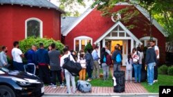 FILE - Immigrants gather with their belongings outside St. Andrews Episcopal Church, Sept. 14, 2022, in Edgartown, Mass., on Martha's Vineyard. 