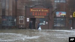 Dua pria berjalan melewati jalanan yang tergenang air di Front Street, yang berjarak beberapa blok dari Laut Bering, di Nome, Alaska, pada 17 September 2022. (Foto: AP/Peggy Fagerstrom)