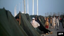 Internally displaced flood-affected people gather outside their tents at a makeshift camp alongside flood waters after heavy monsoon rains in Sukkur, Sindh province, Sept. 5, 2022.
