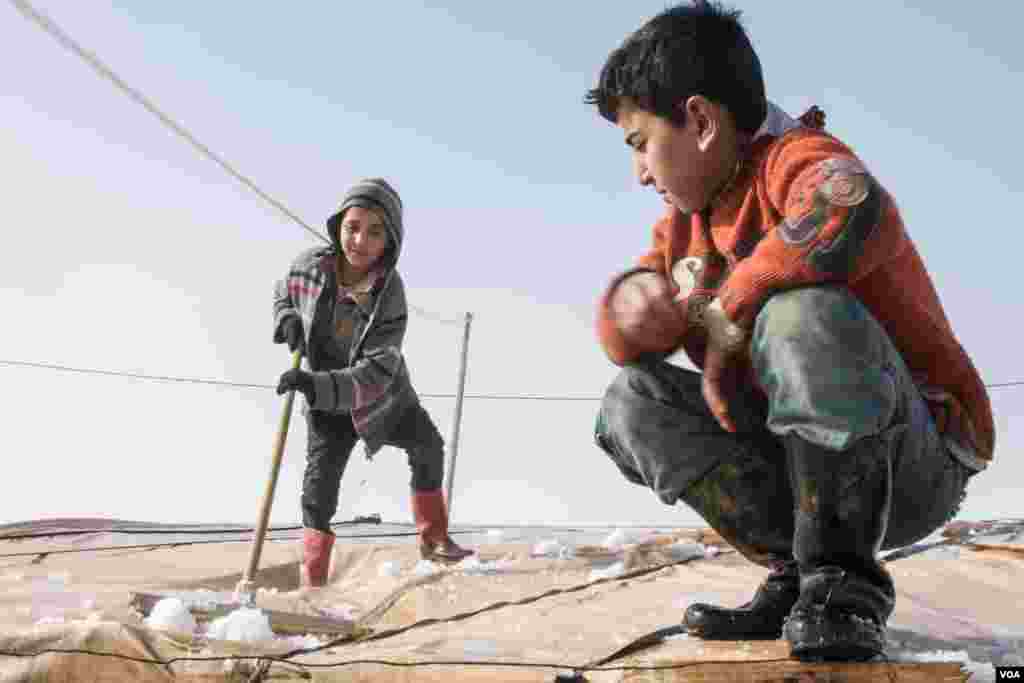 Children sweep snow from the roof of their shelter. Few of the tents are new and run the risk of collapsing under the strain of the weather. (John Owens/VOA News)