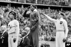 FILE - On Aug. 11, 1936, America's Jesse Owens, center, salutes during the presentation of his gold medal for the long jump, alongside silver medalist Luz Long, right, of Germany, and bronze medalist Naoto Tajima, of Japan, during the Summer Olympics in Berlin.