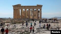 FILE - People visit the ancient Parthenon Temple atop the Acropolis hill archaeological site in Athens, Greece, Feb. 26, 2022.