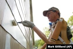 Seorang pengguna robot lengan mendemonstrasikan penggunaan lengan palsu barunya dengan menggunakan roller cat di samping rumahnya. (Foto: AP)