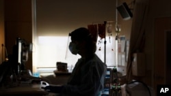 Perawat bekerja di depan komputer sambil membantu pasien COVID-19 di Los Angeles. Banyak rumah sakit Amerika mencari pekerja perawatan kesehatan karena menghadapi kekurangan perawat di tengah pandemi yang berat. (Foto: AP)