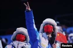 Seorang perempuan mengenakan masker, memegang bendera nasional Cina menjelang upacara pembukaan Olimpiade Musim Dingin Beijing 2022 di Stadion Nasional di Beijing, 4 Februari 2022. (REUTERS/Evelyn Hockstein)