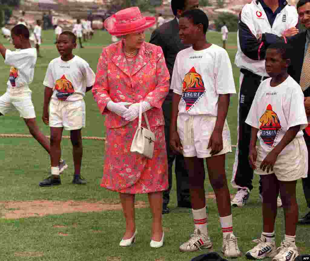 Britain&#39;s Queen Elizabeth talks with young cricketers while on a visit to Alexander Township, north of Johannesburg, South Africa Thursday November 11 1999. The Queen is on a state visit ahead of the Commonwealth Heads of Government Meeting starting Friday in Durban. (Photo by THEMBA HADEBE / AP POOL / AFP)