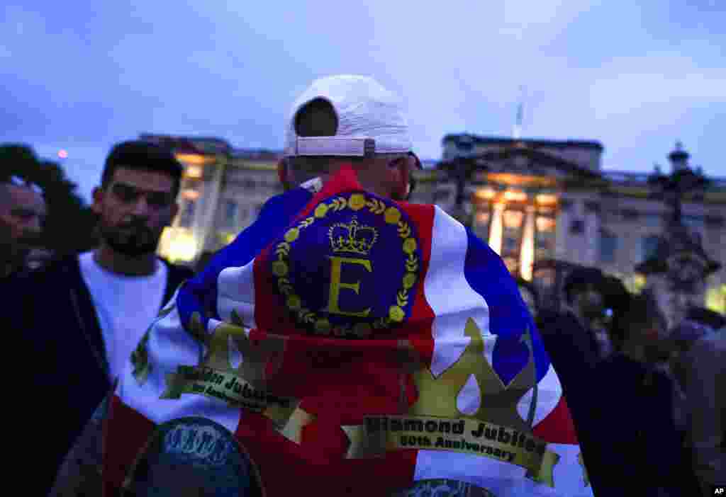 A man wears the Union flag honoring Queen Elizabeth II as he stands in front of Buckingham Palace in London, Sept. 8, 2022.