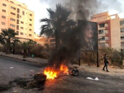 FILE - A man walks near a burning fire blocking a road, during a protest against mounting economic hardships, in Beirut, Lebanon, June 28, 2021.