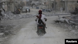 A man drives a motorcycle while carrying his weapon near damaged buildings in the northern Syrian town of al-Bab, Syria, March 1, 2017.