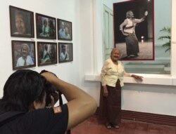 លោក​ស្រី​ព្រឹទ្ធាចារ្យ​ ឯម ធាយ ឈរ​នៅ​ពី​មុខ​រូបថត​របស់​លោក​យាយ ដែល​ជា​ស្នាដៃ​ថត​របស់​លោក Aray Steven ហើយ​ត្រូវ​បាន​ដាក់តាំង​នៅ​សារមន្ទីរជាតិក្នុង​ទីក្រុង​ភ្នំពេញ​នៅ​ថ្ងៃទី៦ ខែវិច្ឆិកា ឆ្នាំ២០១៥។ (ផន បុប្ផា/VOA)