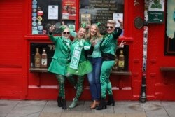 Sejumlah turis berpose di depan pub di Kota Dublin setelah pawai Santo Patrick dibatalkan untuk mencegah penyebaran virus corona, 17 Maret 2020. (Foto: AP)