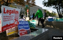 FILE - Pedestrians pass by a D.C. Cannabis Campaign sign in Washington, Nov. 4, 2014.